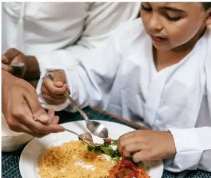 Niño comiendo pasta con la mano de un adulto sirviendo.