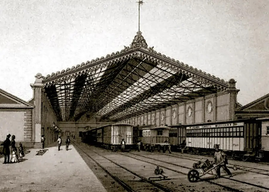 Litografía sepia del interior de la Estación del Ferrocarril de Veracruz: gran nave con techo de hierro y vidrio, vías férreas con vagones de pasajeros y de carga, pasajeros con trajes del siglo XIX y un operario con carretilla de equipajes.