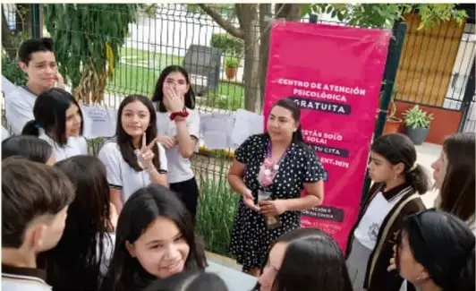 Fotografía de una reunión comunitaria con estudiantes y una persona adulta frente a una manta rosa con texto en español.