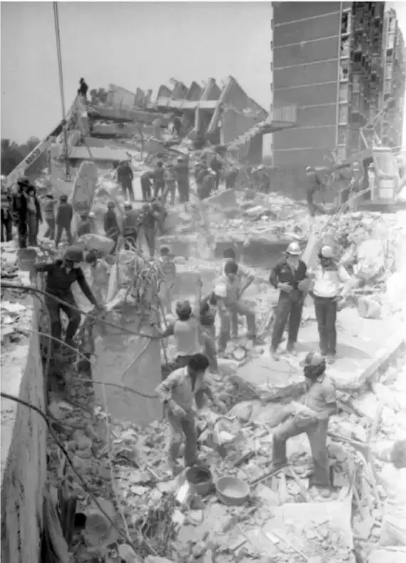 Fotografía en blanco y negro de personas trabajando entre los escombros de un edificio colapsado, con maquinaria y estructuras dañadas, probablemente durante los sismos de 1985 en la Ciudad de México.