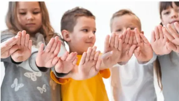 Fotografía de una niña sonriendo mientras junta su palma con la palma de un adulto para comparar el tamaño de sus manos.
