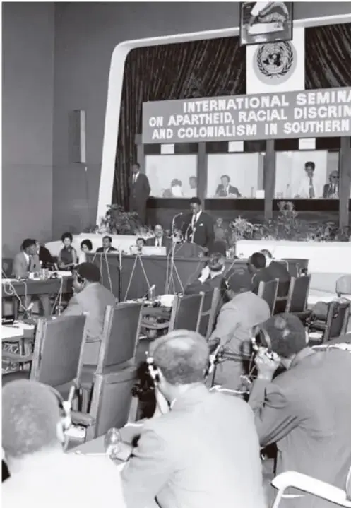 Fotografía en blanco y negro de una sala de conferencias con delegados sentados; al fondo un cartel que dice 'INTERNATIONAL SEMINAR ON APARTHEID, RACIAL DISCRIMINATION AND COLONIALISM IN SOUTHERN AFRICA'.