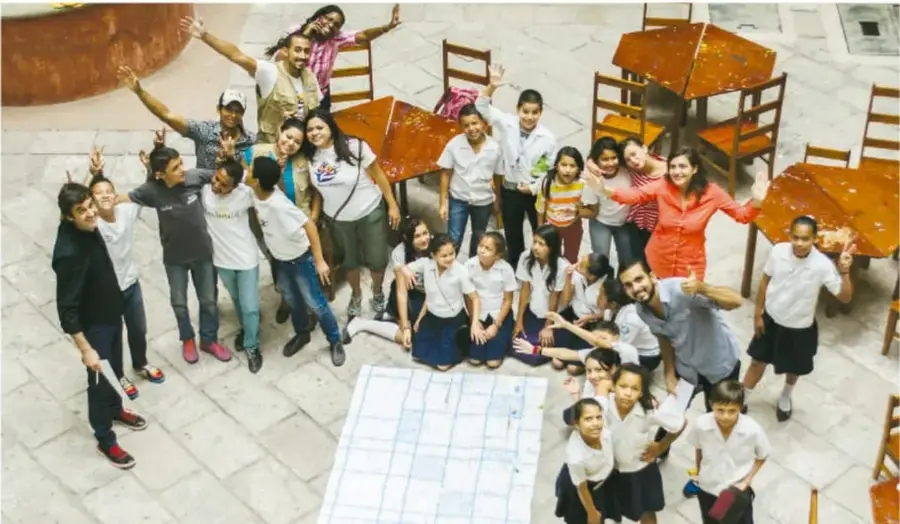 Grupo numeroso de estudiantes y docentes reunidos en un patio, con los brazos levantados, celebrando el festival escolar.