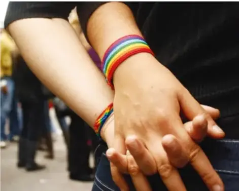 Fotografía de dos personas tomadas de la mano; una de ellas lleva pulseras de colores del arcoíris, símbolo de la diversidad y la inclusión.