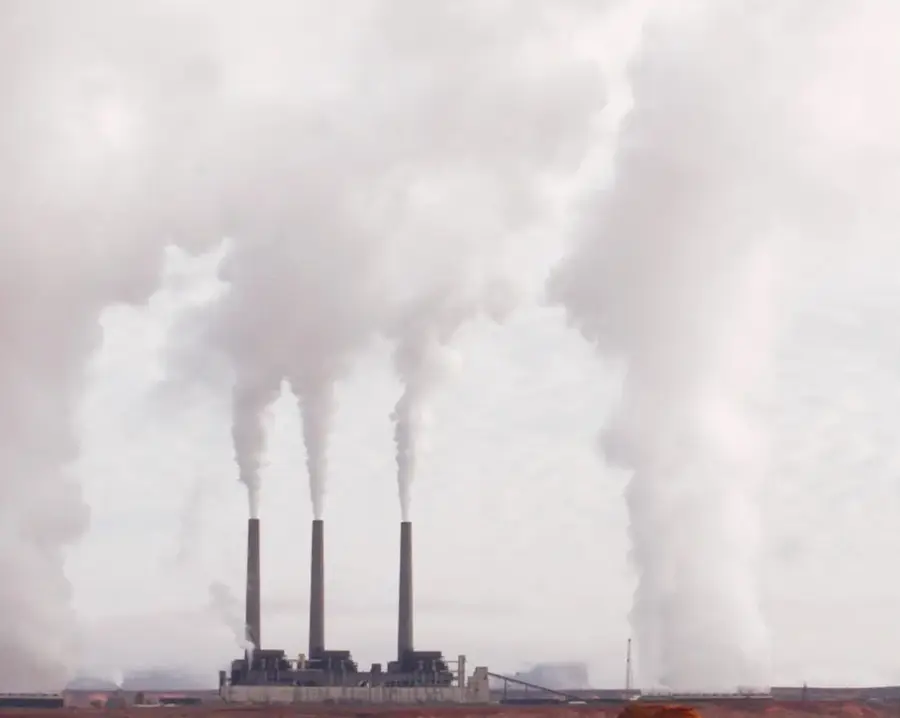 Central eléctrica o industrial con tres chimeneas altas que lanzan enormes columnas de humo blanco y gris al cielo.
