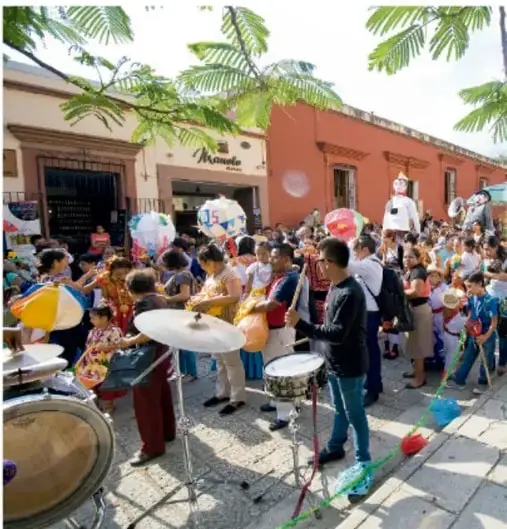 Fotografía de una verbena popular en la calle: música con tarolas y tambores, globos y mucha gente frente a edificios coloniales; representa la participación comunitaria y el impacto de una campaña.