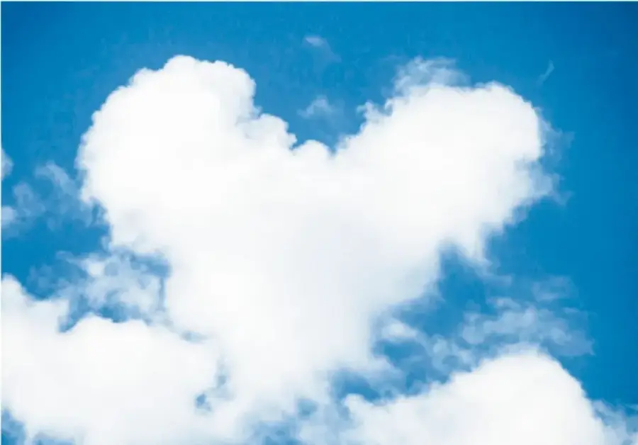 Fotografía de una nube blanca con forma de corazón en un cielo azul con otras nubes dispersas.