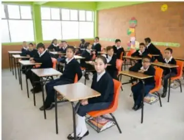 Aula con estudiantes uniformados sentados en sus pupitres durante una clase.