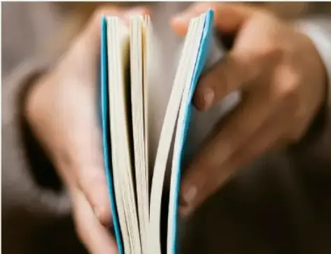 Fotografía de las manos de una persona sosteniendo un libro abierto, con las páginas visibles en primer plano, ilustrando la lectura de la obra literaria.