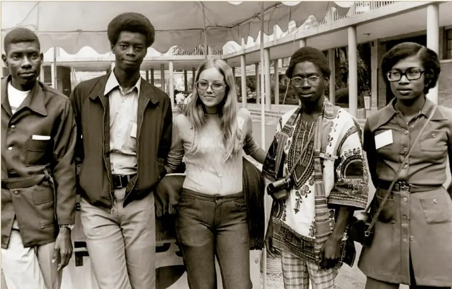 Fotografía en blanco y negro titulada 'Grupo de estudiantes de intercambio, ca. 1970': cinco jóvenes de pie frente a un edificio con columnas y toldo, cuatro de ellos afrodescendientes y una joven caucásica de cabello largo; Archivo Gráfico de El Nacional, Acervo INEHRM.