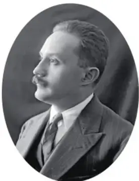 Retrato en blanco y negro de un hombre con bigote, traje y corbata, de perfil.