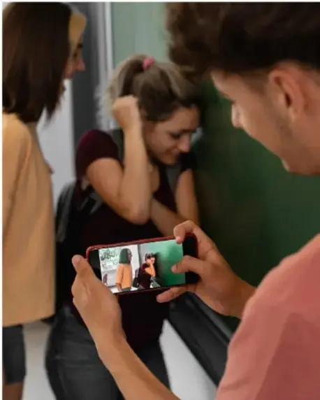 Escena de acoso escolar en un salón: una chica molesta a otra que cubre su rostro mientras un compañero graba el incidente con un teléfono celular.