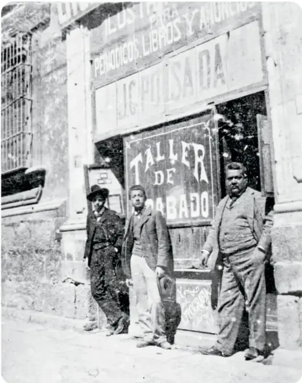 Fotografía antigua en blanco y negro de la fachada de un taller de grabado con el letrero 'J. G. Posada' y tres hombres de traje de la época frente a la puerta.
