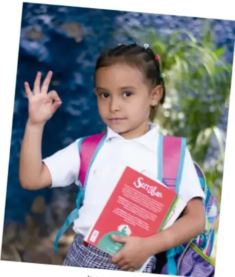 Fotografía de un niño de playera blanca y shorts verdes que celebra de rodillas sobre el pasto con los puños en alto y gran sonrisa, expresando alegría.
