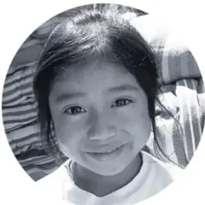 Fotografía en blanco y negro de una niña sonriente, probablemente estudiante participante en el proyecto comunitario, recortada en forma ovalada.