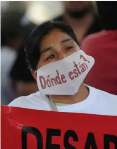 Fotografía de una mujer con cubrebocas blanco que dice '¿Dónde están?' sosteniendo un cartel rojo con la palabra 'DESAPARECIDOS'. Representa la protesta social por los desaparecidos en México.