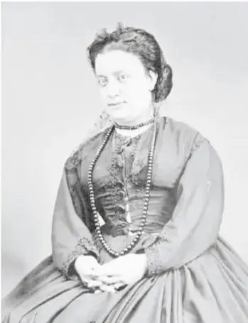 Fotografía en blanco y negro de la cantante de ópera Ángela Peralta, sentada, con vestido oscuro de época y collares de perlas.