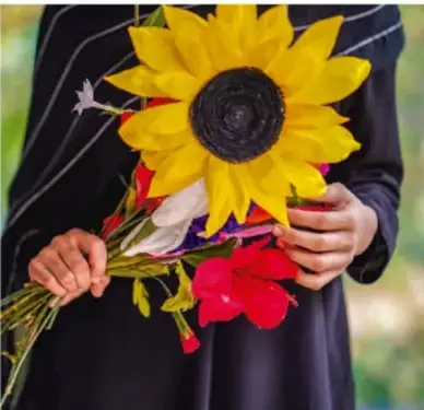Persona sostiene un ramo de flores con un gran girasol y flores rojas.