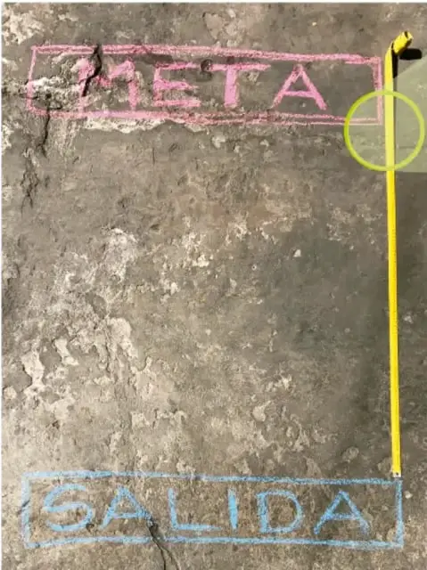 Pista de gis con las palabras META y SALIDA y un flexómetro amarillo midiendo la distancia.
