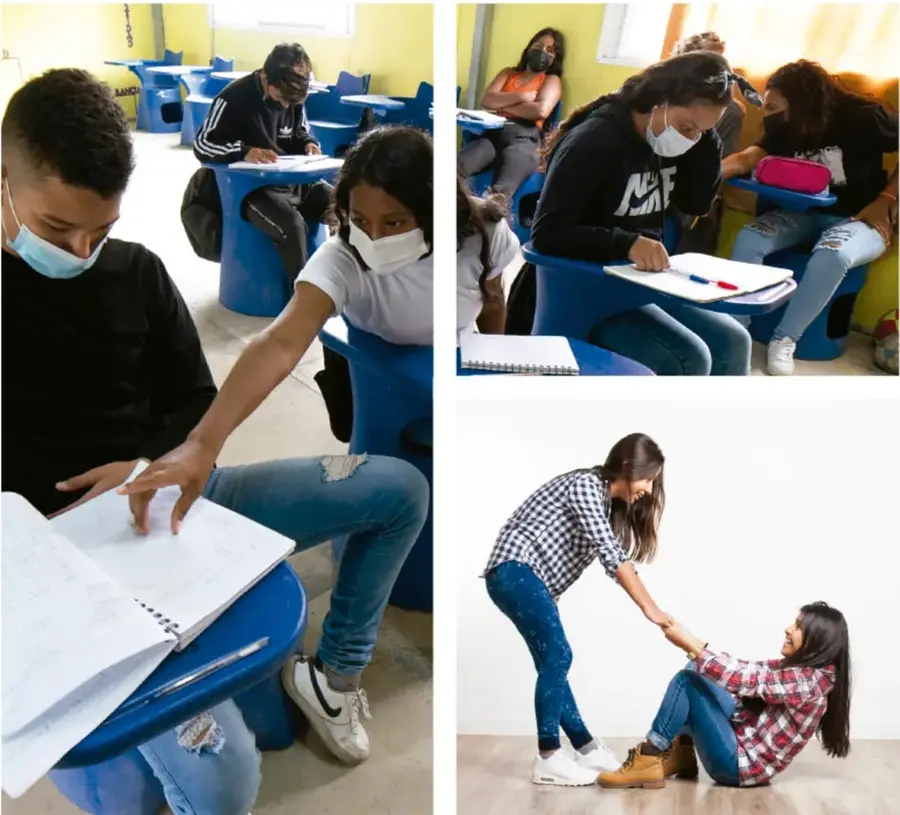 Estudiantes con cubrebocas trabajando en cuadernos en pupitres azules dentro del aula.