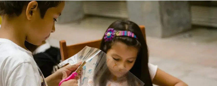 Niño y niña trabajando con tijeras y papel transparente, preparando material para una presentación.