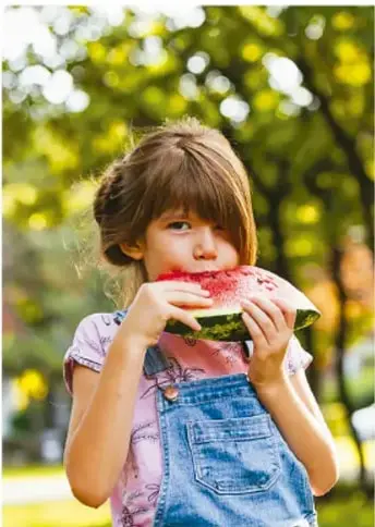 Niña comiendo un trozo de sandía al aire libre.