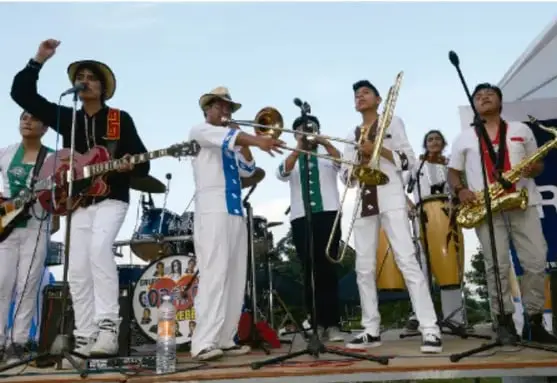 Fotografía de un grupo musical en escenario al aire libre: integrantes con instrumentos de viento (trompetas), guitarras y atuendos tradicionales indígenas junto a ropa urbana. Crédito: Salatiel Barragán Santos, Veracruz.