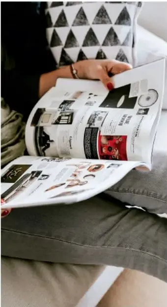 Persona sentada sosteniendo un periódico desplegado con artículos e imágenes, ilustrando el acceso a la información por medios de comunicación.