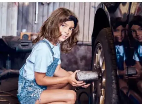 Niña cambiando la llanta de un automóvil, realizando una actividad tradicionalmente asociada a los hombres.