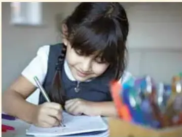 Niña escribiendo en su cuaderno con lápiz, sonriendo.