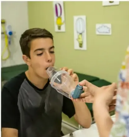Fotografía de un adolescente utilizando un inhalador para el asma, asistido por otra persona.