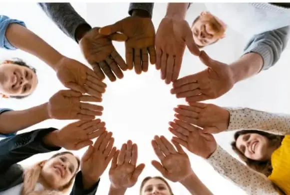 Fotografía cenital de un grupo de personas formando un círculo con sus manos extendidas hacia el centro, símbolo de convivencia y contacto entre culturas.