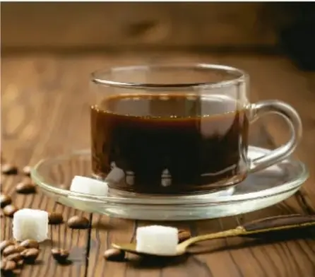 Taza de café con terrones de azúcar y granos de café sobre una mesa de madera.