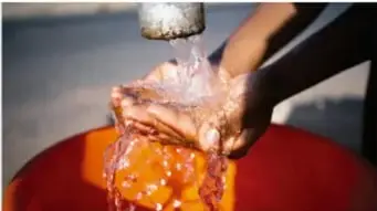 Manos bajo un chorro de agua, ilustrando el consumo de agua para cultivar algodón.