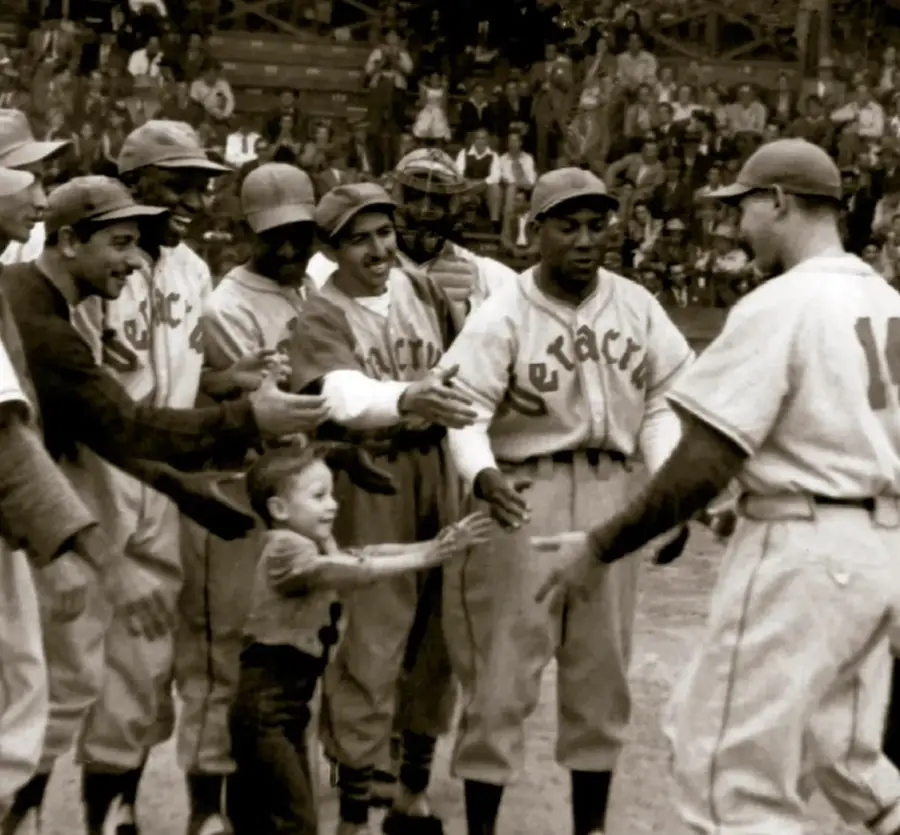 Fotografía histórica en sepia de jugadores de béisbol del Águila de Veracruz (ca. 1940) celebrando en el campo, junto a un niño; los uniformes llevan escrito 'Veracruz'. Un jugador afrodescendiente destaca en el centro.