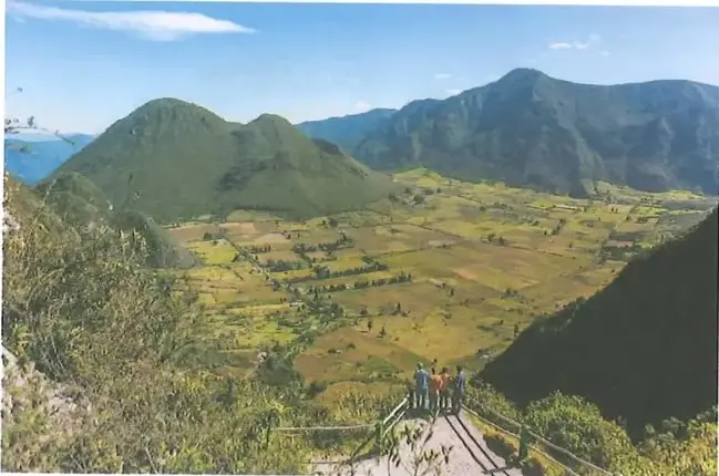 Paisaje de la Reserva Geobotánica Pululahua, con montañas, cultivos y un sendero.