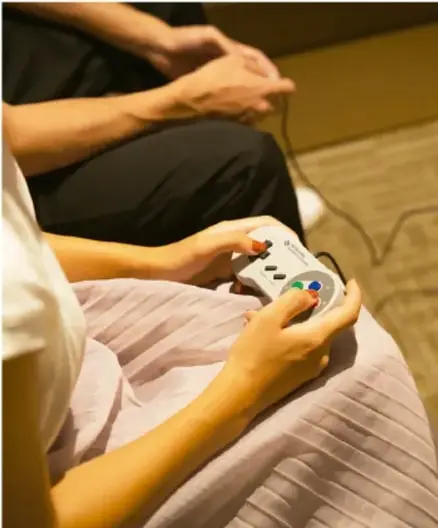 Fotografía de personas sentadas; una sostiene un mando de videojuegos, ilustrando sedentarismo o actividades de ocio en jóvenes.