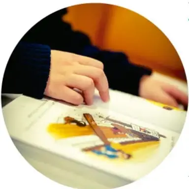 Manos de una niña o niño tomando notas con colores junto a materiales impresos, acompañado por un adulto.
