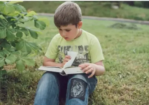 Niño leyendo un libro al aire libre, sentado en el pasto.