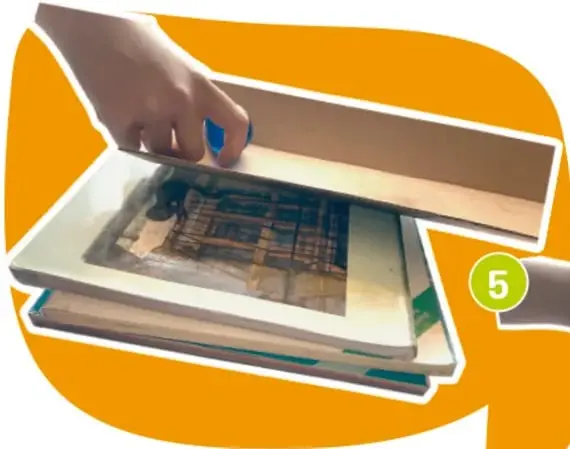Manos colocando libros debajo de una rampa con una canica.
