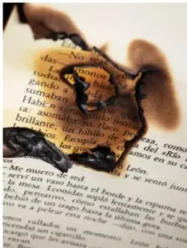 Fotografía de libros abiertos y apilados en una mesa, con volúmenes rojos de fondo, junto a un libro antiguo ilustrado.