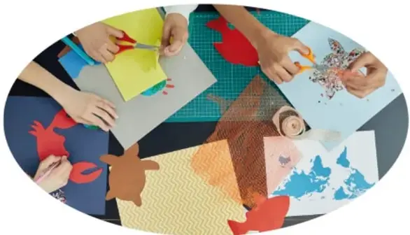 Fotografía de manos de varias personas recortando y armando figuras de colores (papel, telas, animalitos) sobre una mesa de trabajo, ilustrando la actividad práctica de describir a través de apoyos visuales.