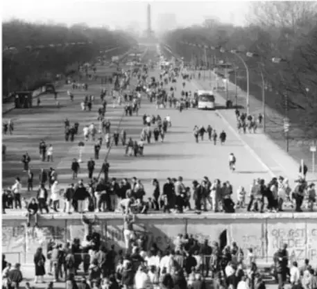 Fotografía histórica en blanco y negro de una multitud caminando y observando el muro de Berlín, símbolo de la división del mundo bipolar.