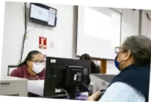 Fotografía de una persona siendo atendida en una oficina o módulo de servicios, con una computadora y una ventanilla.