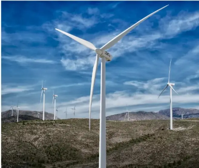 Fotografía de varios aerogeneradores de energía eólica en un paisaje árido con cielo azul y nubes, enmarcada en un rectángulo.