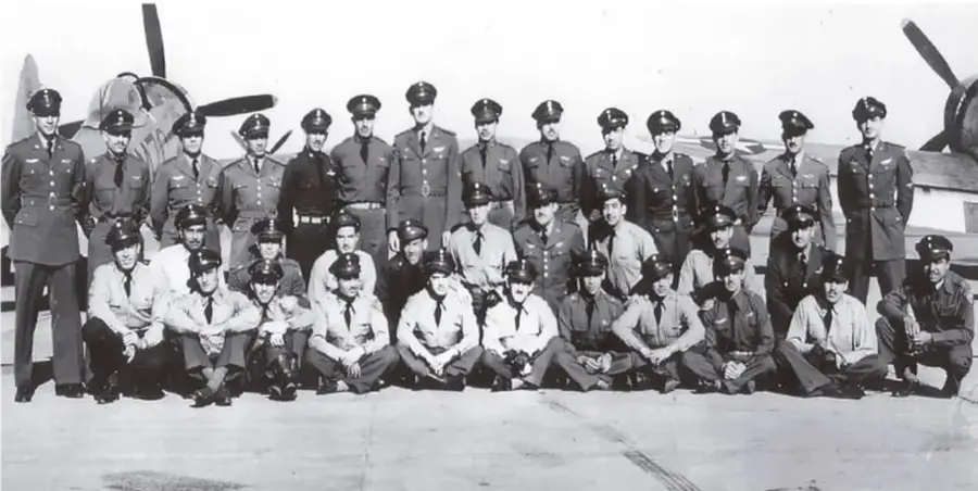 Fotografía en blanco y negro de un grupo numeroso de militares mexicanos, algunos de pie y otros agachados, posando frente a un avión de la Fuerza Aérea Mexicana. Los militares visten uniformes de gala y de campaña.