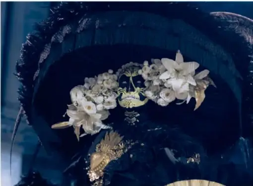 Fotografía de una pieza decorativa oscura adornada con flores blancas y detalles dorados.