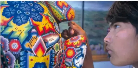 Fotografía de una persona observando de cerca una prenda bordada con flores y figuras de colores vivos, ejemplo de artesanía textil mexicana.