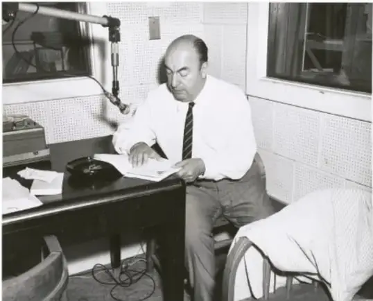 Fotografía en blanco y negro de un hombre (posiblemente un escritor o intelectual) sentado frente a un micrófono de radio, leyendo o escribiendo en documentos sobre una mesa; probablemente un autor posvanguardista en un estudio de radio.