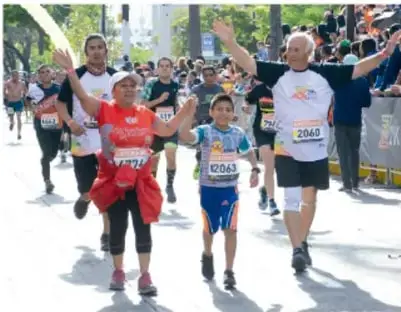 Fotografía de una carrera pedestre con adultos y niños participando, algunos con brazos levantados.